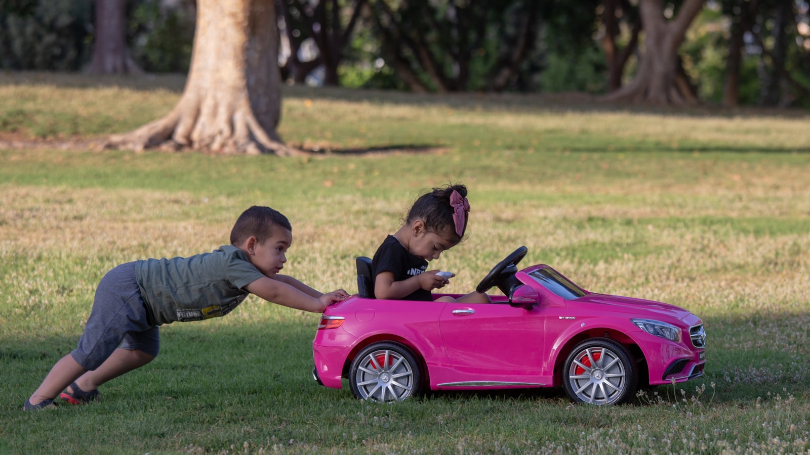 two children playing with a pink toy car